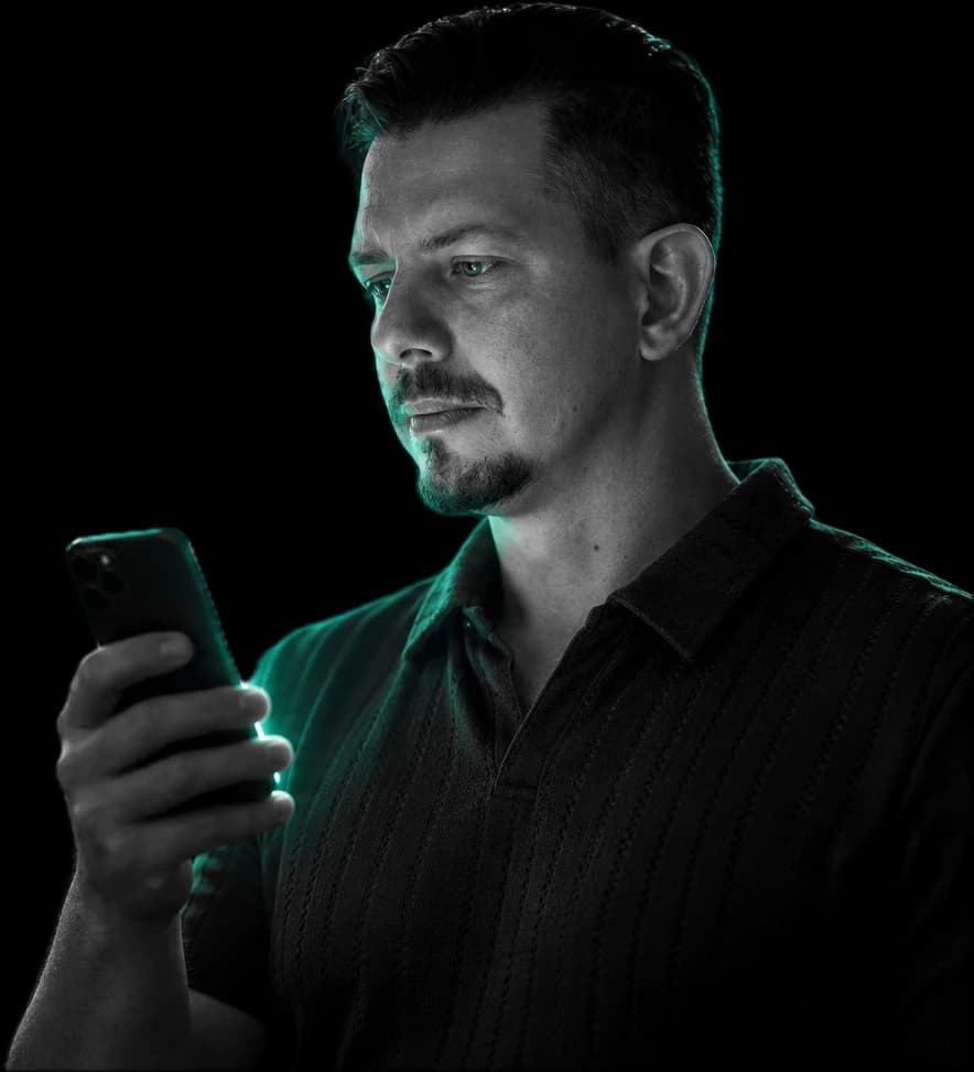Miroslav Krídl číta v mobile správu o novom dopyte (portrét upravený pomocou AI)